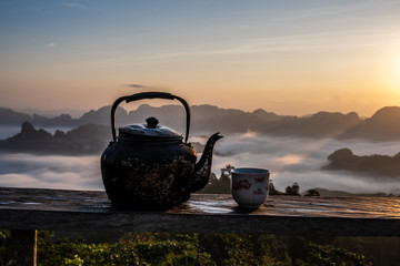 Old kettle and tea cup on mist and mountain background.