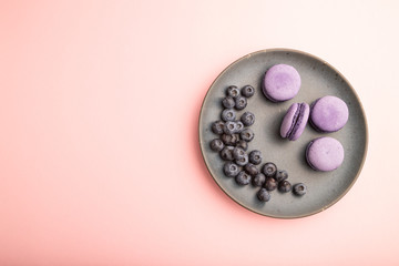 Purple macarons or macaroons cakes with blueberries on ceramic plate on a pastel pink background. Top view, copy space.