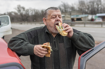 Portrait of Caucasian senior driver being delighted while gobbling lyulya kebab in lavash near his...