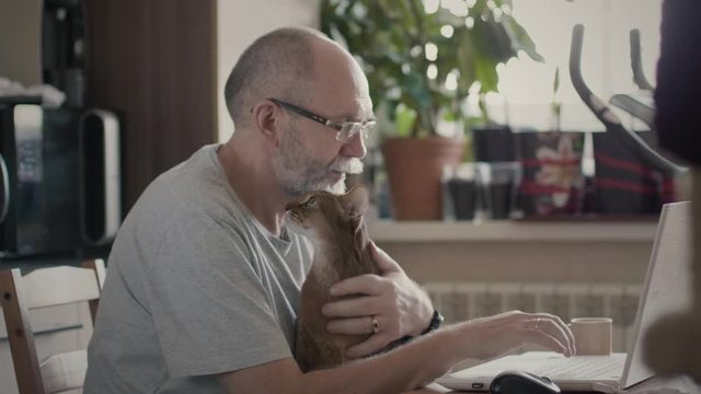 Old man working on a laptop holding pet
