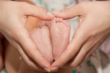 a small newborn baby in the arms of its mother, the mother holds the newborn's legs in her hands