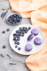 Purple macarons or macaroons cakes with blueberries on white ceramic plate on a gray concrete background. Side view.