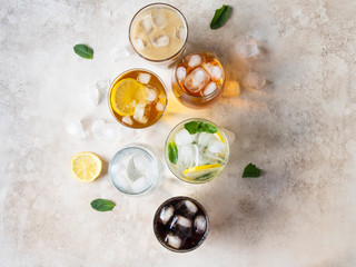 Flat lay of various refreshing drinks in glasses with ice. Apple juice, cola, homemade lemonade, iced coffee, iced tea and sparkling water on a beige background. Top view