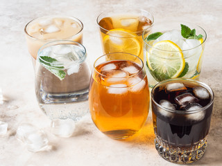 Various refreshing drinks in glasses with ice. Apple juice, cola, homemade lemonade, iced coffee, iced fruit tea and sparkling water on a beige background. Copy space