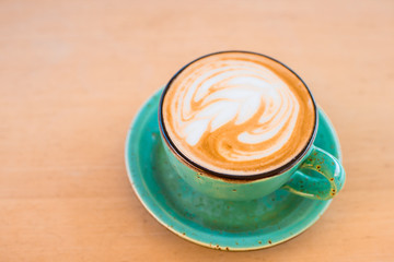 One cup of cappuccino with latte art on wooden background, greenery ceramic cup, place for text