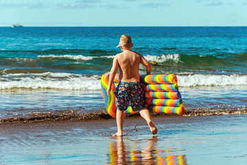 Beach holidays and sports. A boy with a colored air mattress runs into the sea