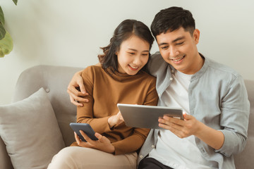 leisure, technology and internet addiction concept - happy couple with tablet computer and smartphone at home