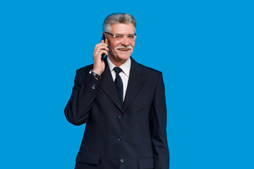 Cheerful elderly gray-haired mustache bearded man in classic suit posing isolated on blue background in studio