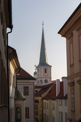 Fototapeta na wymiar view of a Prague street, narrow street, light colored buildings with reddish roofs in the background highlights the pointed roof of a church