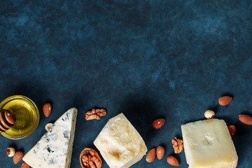 Various sorts of cheese, nuts and honey at the bottom side on the dark blue textured background. Copy space for text and top view