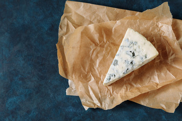 Blue cheese on a parchment paper. Dark textured background, top view