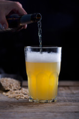 Man pouring craft beer into glass, dark wooden background