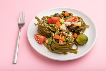 Tagliatelle green spinach pasta with tomato, pea and microgreen sprouts on a pastel pink background. Side view.
