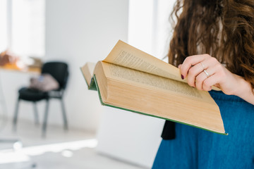 Young adult girl reading book near the window.