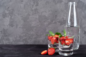 Infused water with strawberry and mint in sparkling glasses on wood black table background, copy space. Cold summer drink. Mineral water