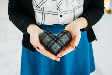 Picture of a small  heart in hands, female holds handmade sewn soft toy, woman with Valentine gift against the window, happy girl smiling, conceptual image of health care or love.