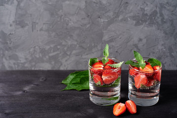 Infused water with strawberry and mint in sparkling glasses on wood black table background, copy space. Cold summer drink. Mineral water