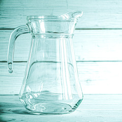 An empty glass carafe for water stands on a white wooden background