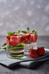 Water with strawberry and mint in sparkling glasses on gray napkin on concrete table, copy space. Cold summer drink. Mineral water