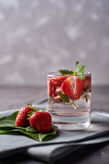 Water with strawberry and mint in sparkling glasses on gray napkin on concrete table, copy space. Cold summer drink. Mineral water