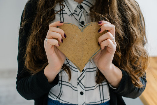 A Young Woman Holds Out A Cut Out Construction Paper Heart Near The Window.