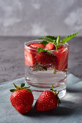 Water with strawberry and mint in sparkling glasses on gray napkin on concrete table, copy space. Cold summer drink. Mineral water