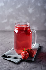 Homemade strawberry tea with mint in mason jar on gray concrete table background, copy space. Cold summer berry drink in sparkling glasses. Fresh vitamin beverage