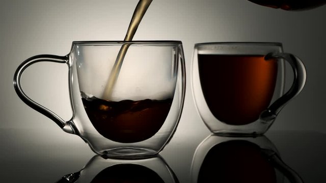 Black tea is poured into a glass cup on a white background
