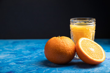 Glass of orange juice on a black and blue background. Side view, copy space.