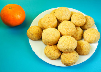 On a white plate are round biscuits made from almond nuts, eggs, butter, corn and buckwheat flour next to an orange mandarin on a turquoise background.  Gluten free