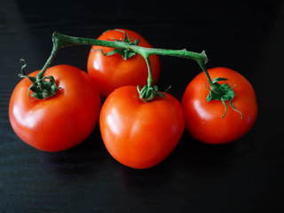 Four round red tomatoes on a black background. Macro vegetables