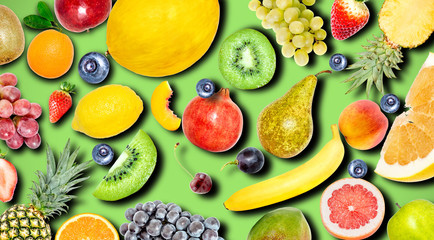 Creative photo of many different exotic tropical bright fruits with shadows on a green summer background. View from above. Bright summer fruit pattern.