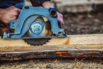 Circular saw for cutting boards into the hands of the builder, the man sawed bars, construction and home renovation, repair and construction tool. Carpenter Using Circular Saw for wood. Close-up