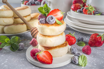 Cottage cheese pancakes with honey and various summer berry on grey background, summer breakfast or lunch