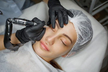Permanent make up eyeliner procedure, applying on young girl. Close-up. Young beautiful woman...