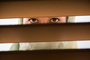 Lonely muslim young woman in a headscarf looks through the wooden blinds. Concept
