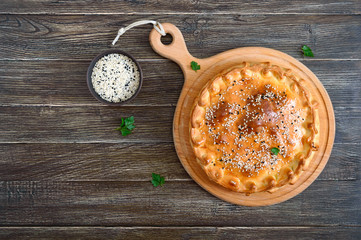 Cabbage pie. Tasty freshly baked homemade vegetable pie with cabbage, spinach, eggs and sesame seeds on a wooden board. Top view.