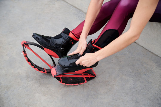Close-up picture of hands in the process of buttoning kangoo jumps. Young woman's legs, wearing magenta leggings, putting on kangoo jumps shoes, preparing for fitness training