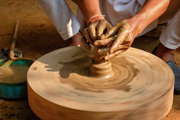 Pottery - skilled hands of potter shaping the clay on potter wheel making small bottle. Pot throwing. Manufacturing traditional handicraft Indian jar, pot, jug. Shilpgram, Udaipur, Rajasthan, India
