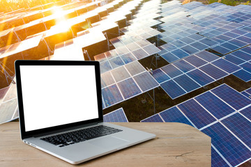 Laptop with blank screen on table. Beautiful sunset over Solar Farm with sunset on the background