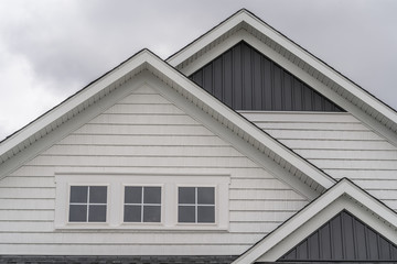 Triple gable facade with thick white frame triple attic window, white horizontal vinyl siding, dark vertical siding on a new construction East Coast American single family home