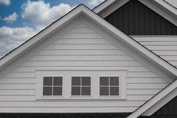Closeup triple gable facade with thick white frame triple attic window, white horizontal vinyl...