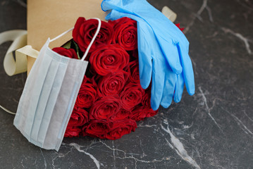 contactless delivery - face mask medical glove and bouquet of red roses, the concept of quarantine and isolation during the coronavirus pandemic and the decline economy of flower businesses and shops