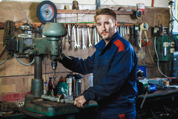 A mechanic drills a detail on a drill press. Workflow mechanic in a car garage. Auto service concept.