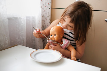 Toddler child girl feeds doll at little table