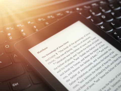 Close up of ebook reader with The Holy Bible on a laptop keyboard, with sun rays light concept