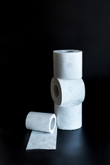 on a black background stands a tower of three rolls of toilet paper and next to it lies an almost finished roll