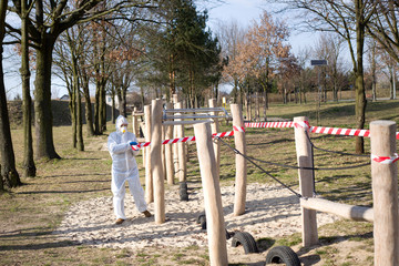 Kobieta w kombinezonie ochronnym ogradza drewniany plac zabaw dla dzieci przy użyciu taśmy bezpieczeństwa