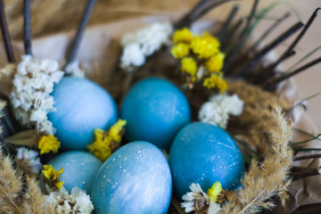 Fototapeta na wymiar Easter holiday, background and decor of painted blue eggs in nest of flowers, branches. Religion and traditions.