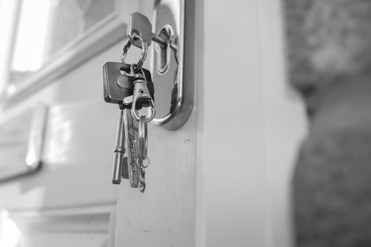  black and white photo of a close up of a house key in the keyhole of a white door with other keys on a ring hanging down